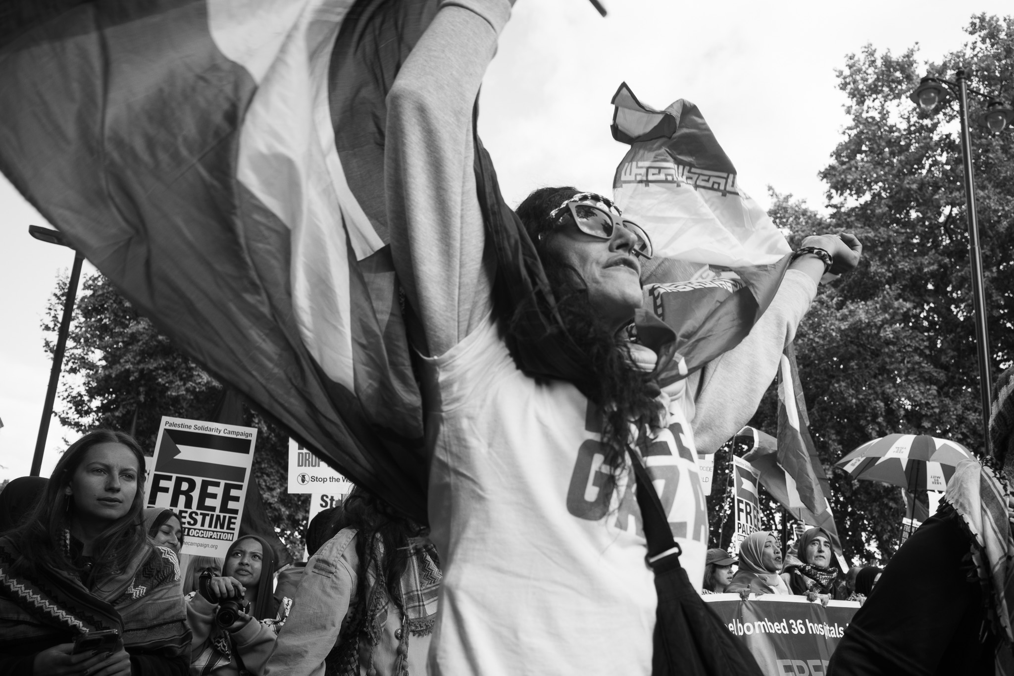 A woman with raised arms holding flags, placards and marchers behind her