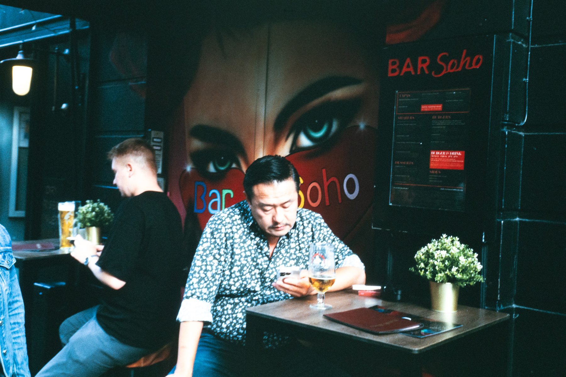 Two men in a Soho bar, one looking at his phone beneath a mural