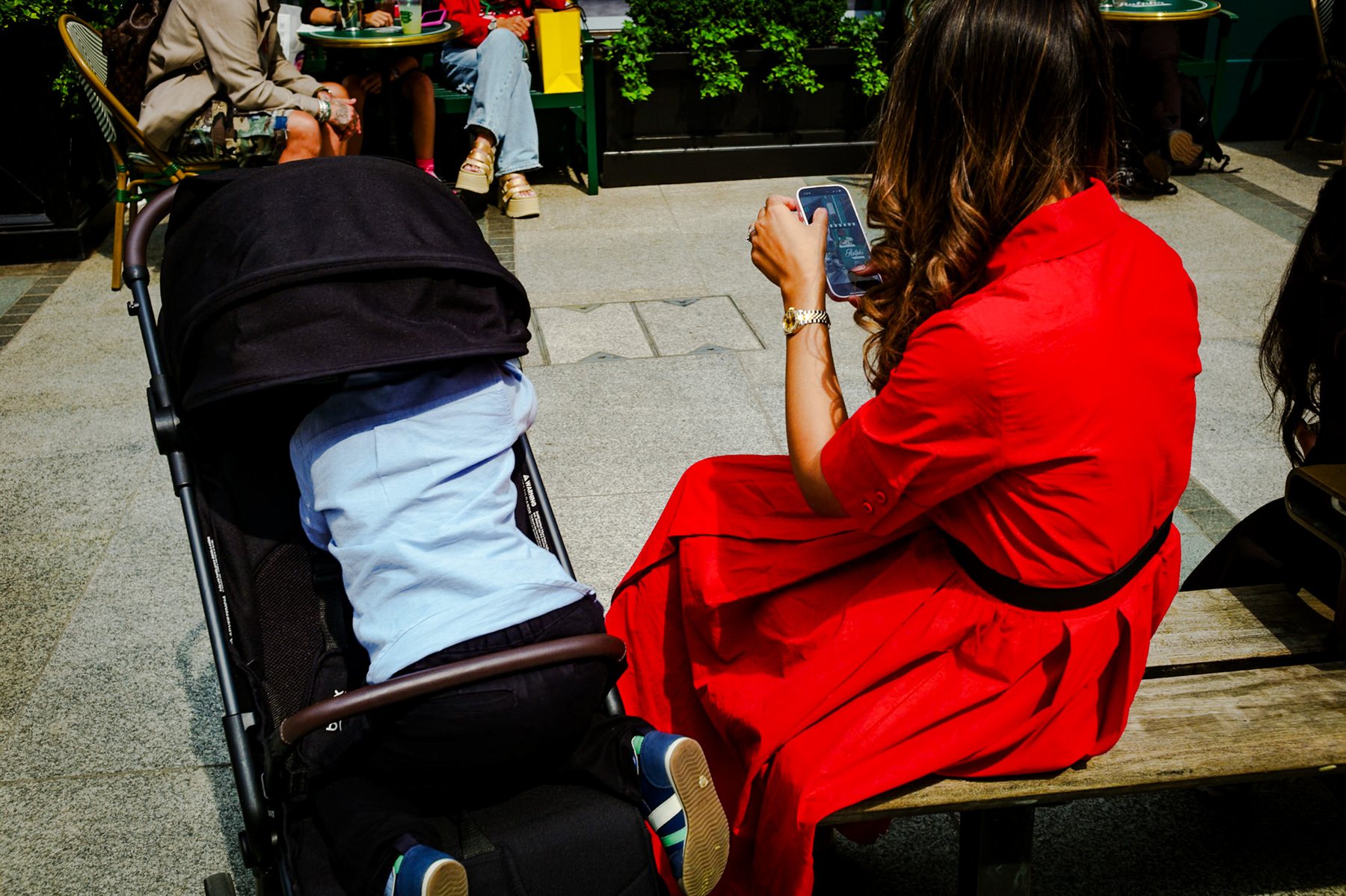 A woman in a red dress on a bench beside a pushchair