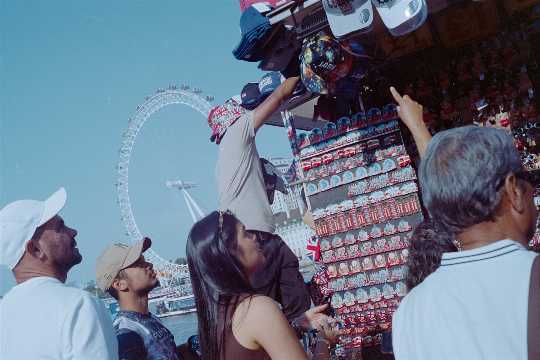 Tourists browsing a souvenir stall with the London Eye behind