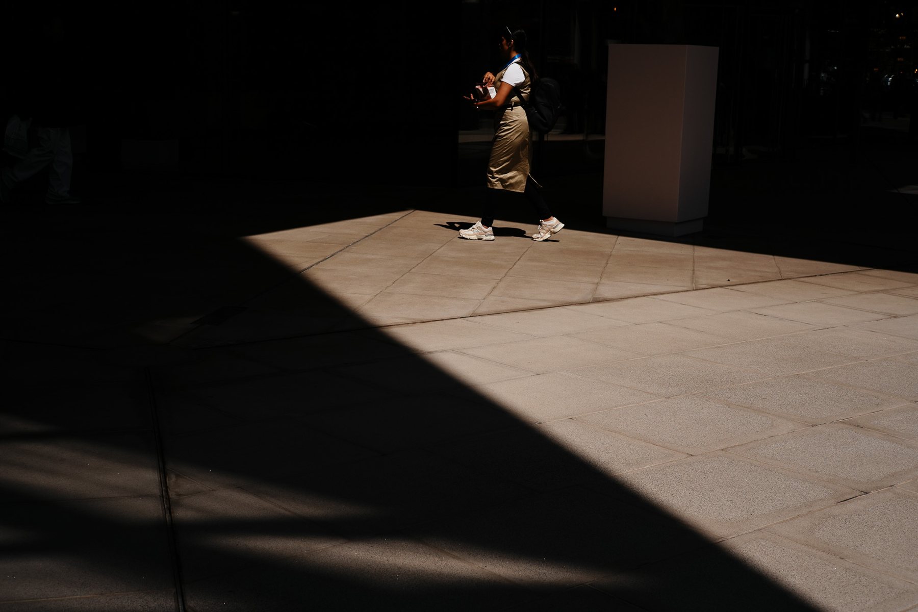A lone figure crossing a sharp patch of light on a paved square