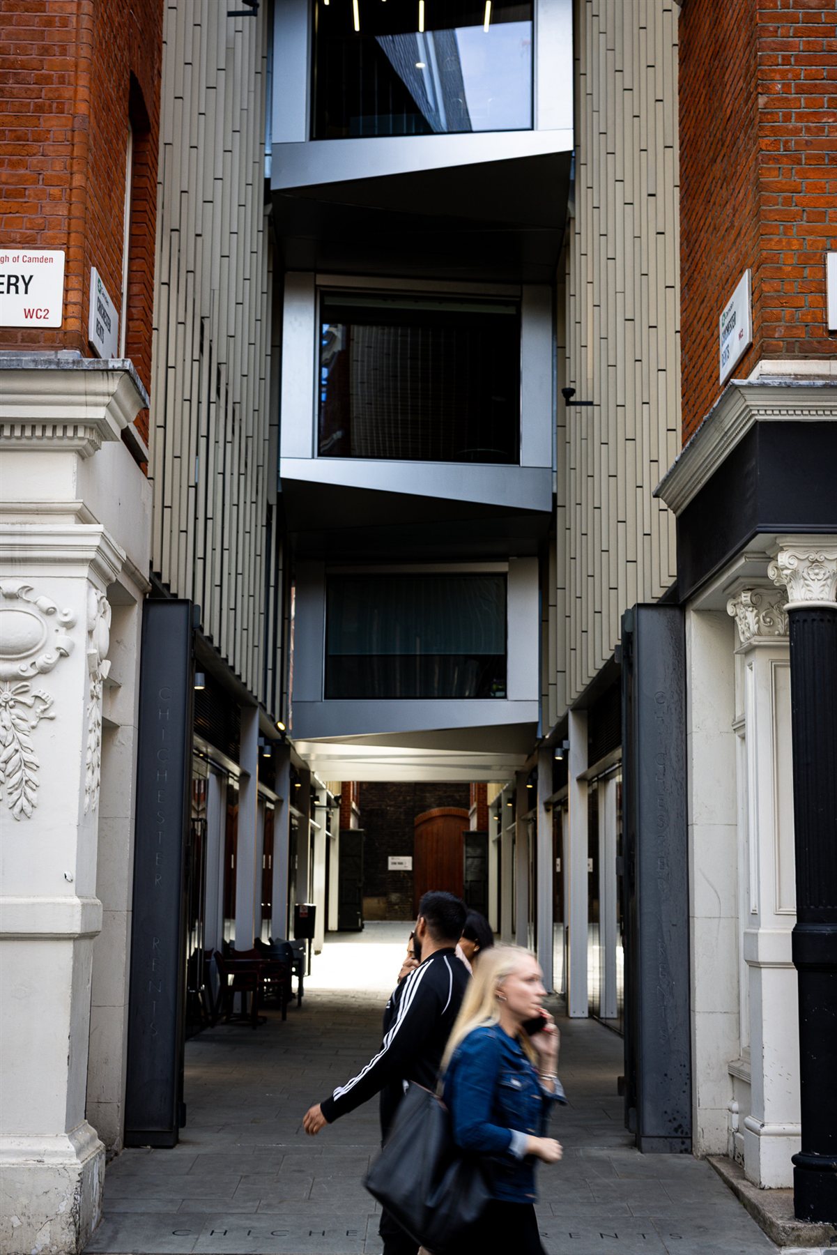 A woman walking through a narrow alley between brick buildings