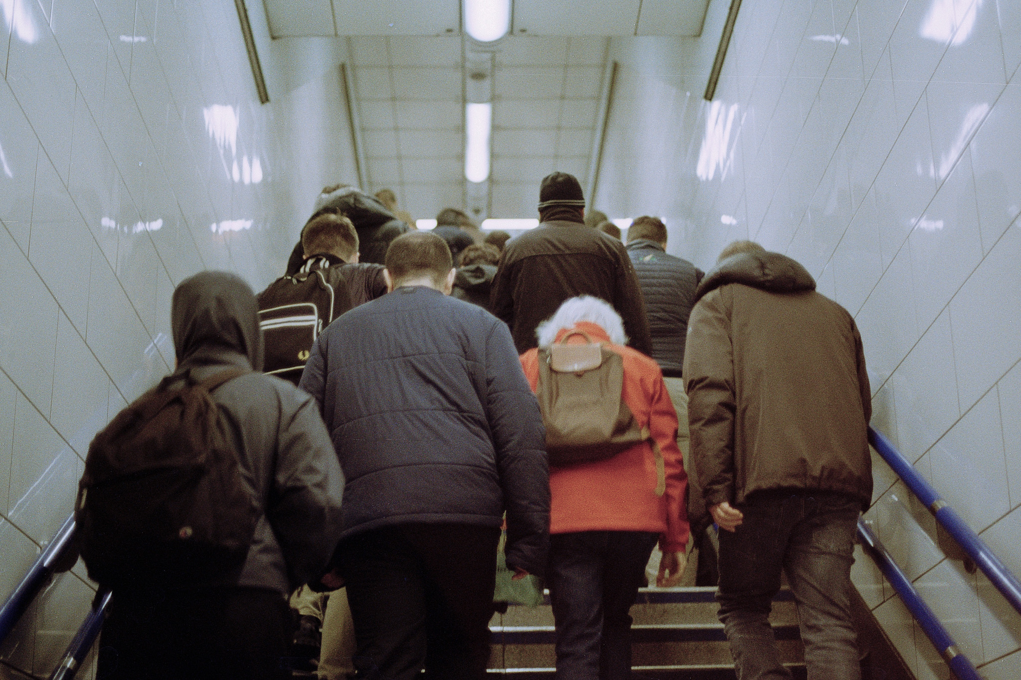 A crowd climbing a staircase seen from behind, one red jacket among dark coats